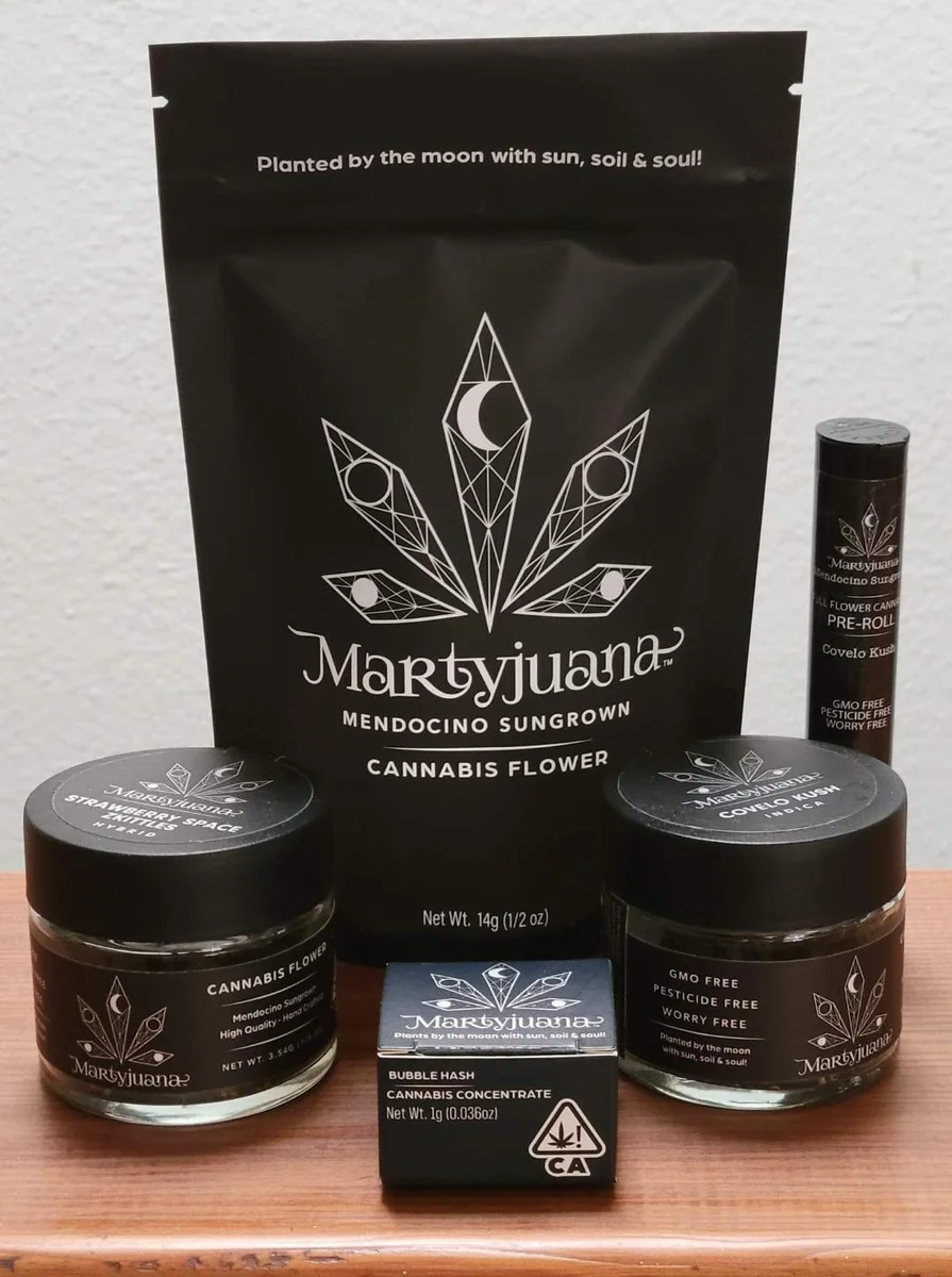 Black Martyjuana packaging with white moon-phase logos on flower pouches, jars, and a pre-roll tube